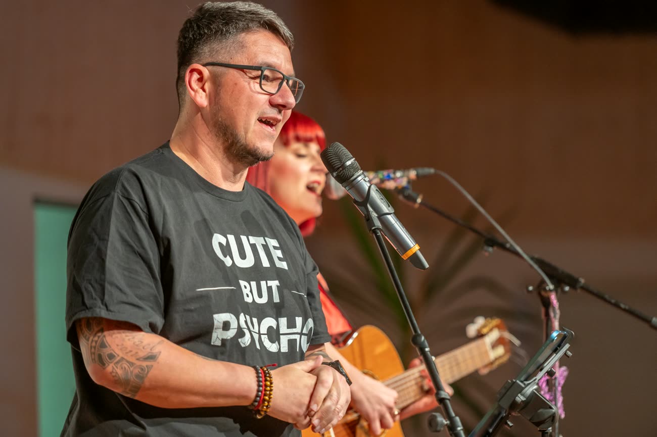 Markus Warscher am Mikrofon, dahinter Daniela Flickentanz mit Gitarre, beim Bühnenprogramm „Mein leises Leben mit einem lauten Tabu.“